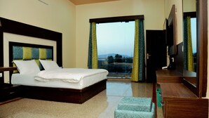 A hotel room with a large bed, a wooden headboard, a television, and a view of the outdoors through a large window.