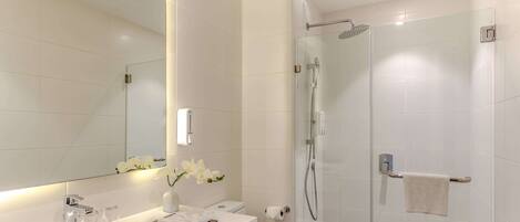 A modern bathroom with a white sink, mirror, and glass shower enclosure.