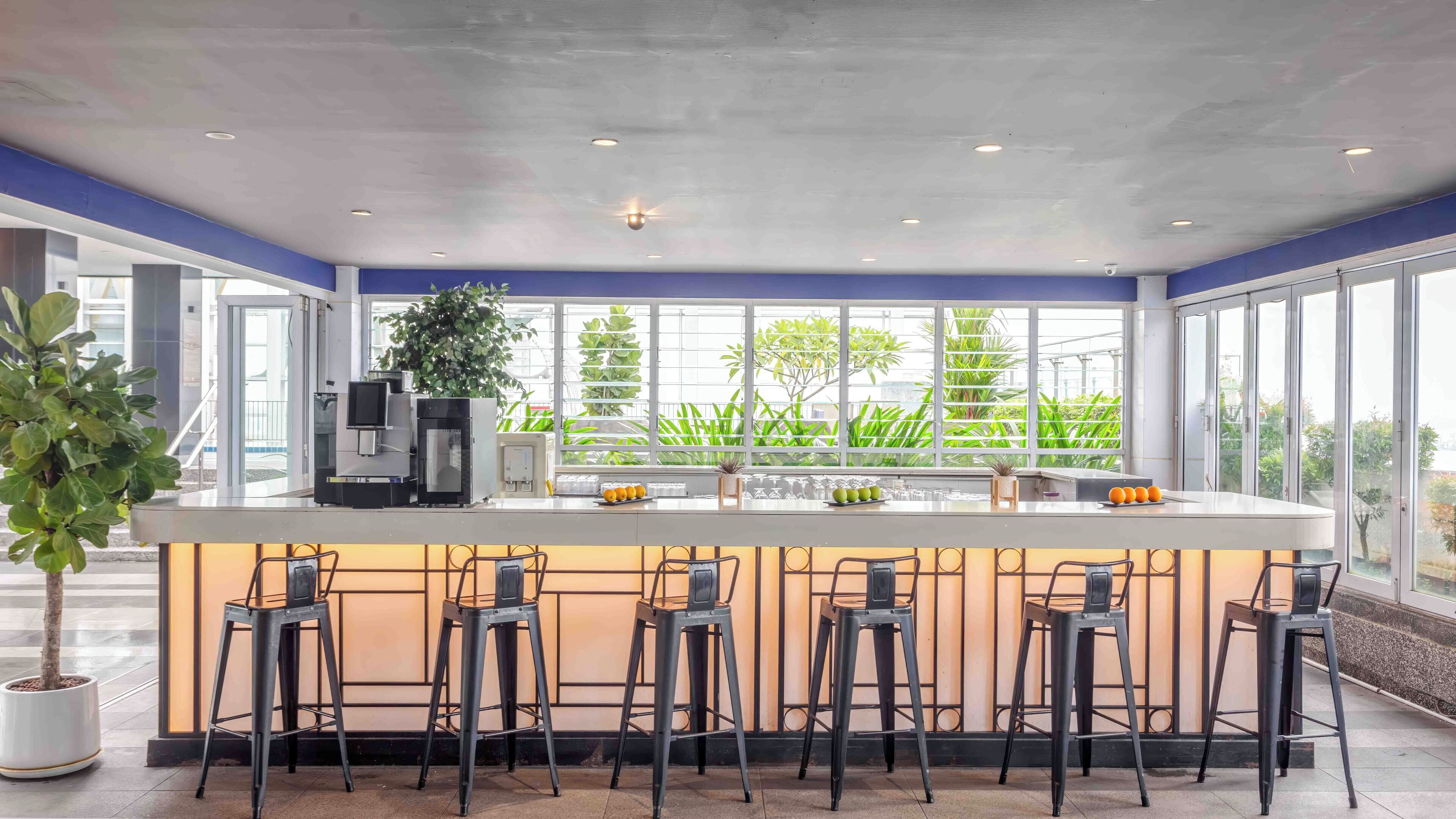 A modern bar area with a central island, bar stools, and large windows offering a view of greenery outside.