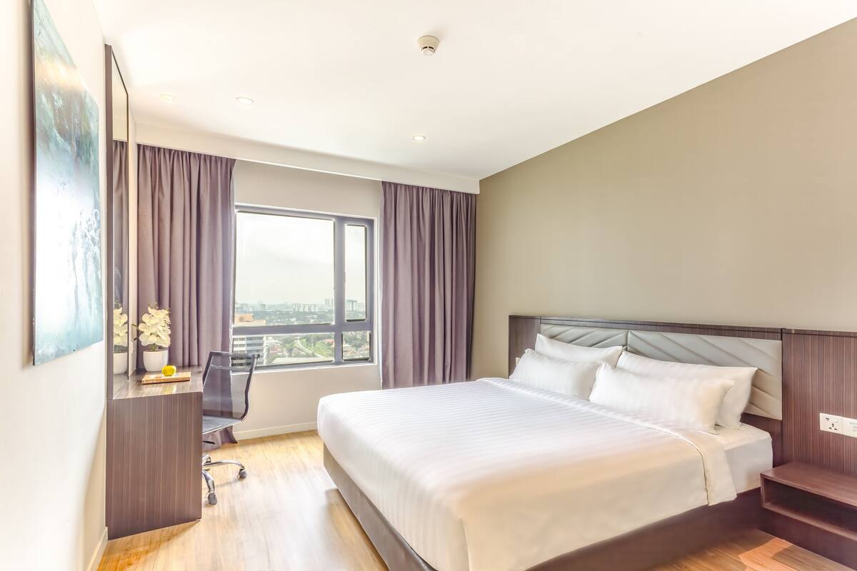 Ein modernes Hotelzimmer mit einem großen Bett, einem Schreibtisch mit Stuhl, einem Fenster mit Vorhängen und Blick auf die Stadt.