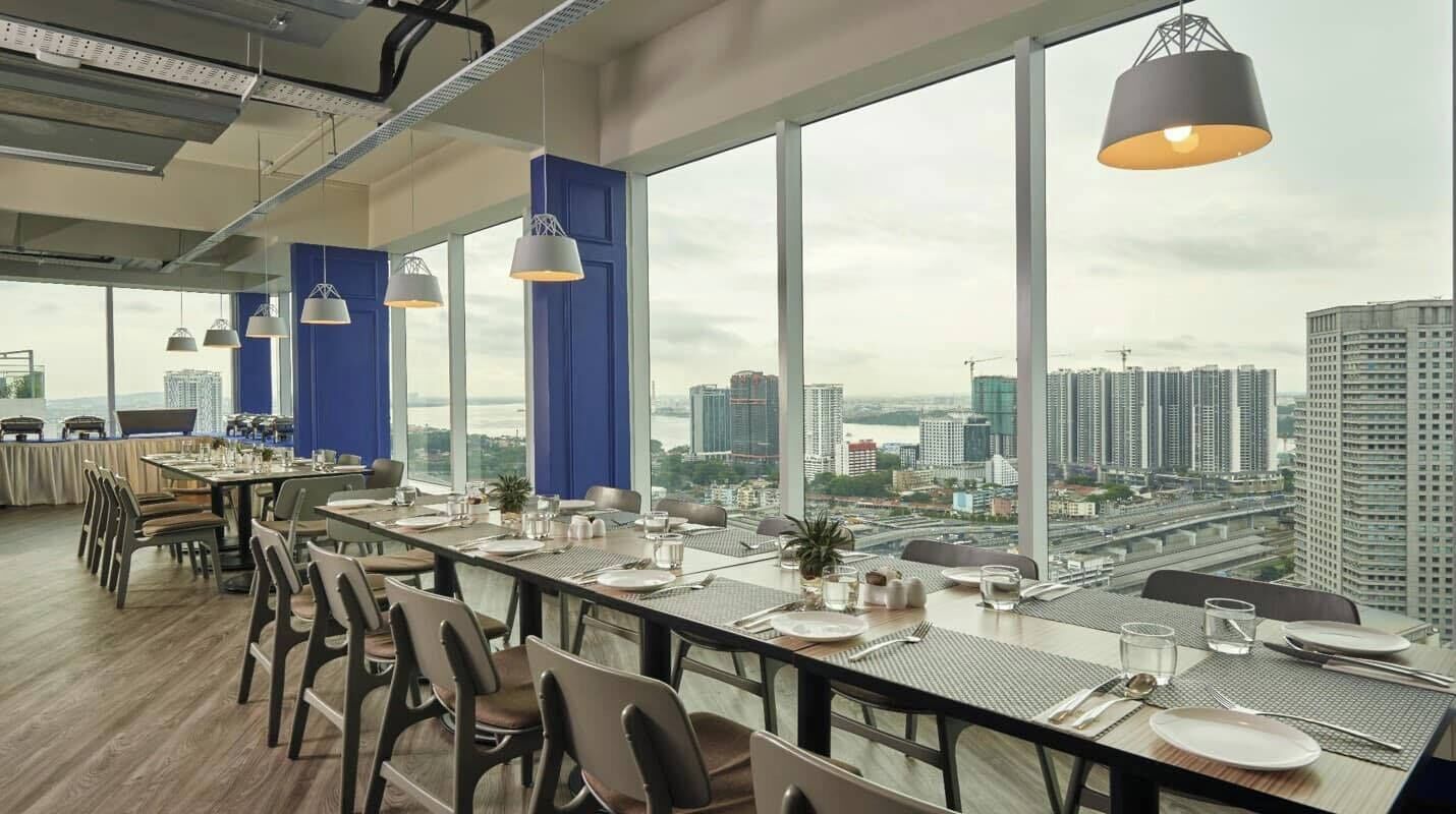 Un comedor moderno con una mesa larga dispuesta para una comida, ventanas amplias con vista a la ciudad e iluminación de estilo industrial.