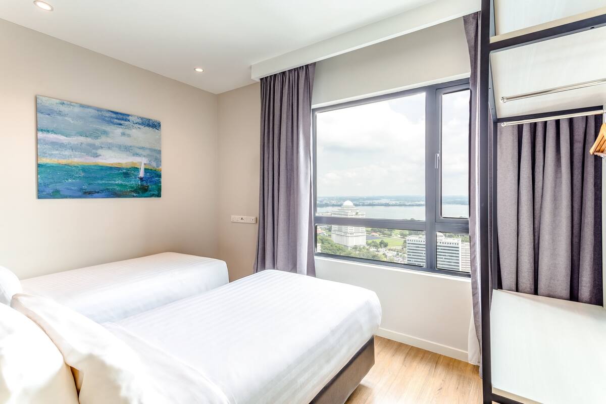 Ein Hotelzimmer mit zwei Betten, einem großen Fenster mit Blick auf eine Stadtansicht, einem Bild an der Wand und einem Schrank mit Spiegel.