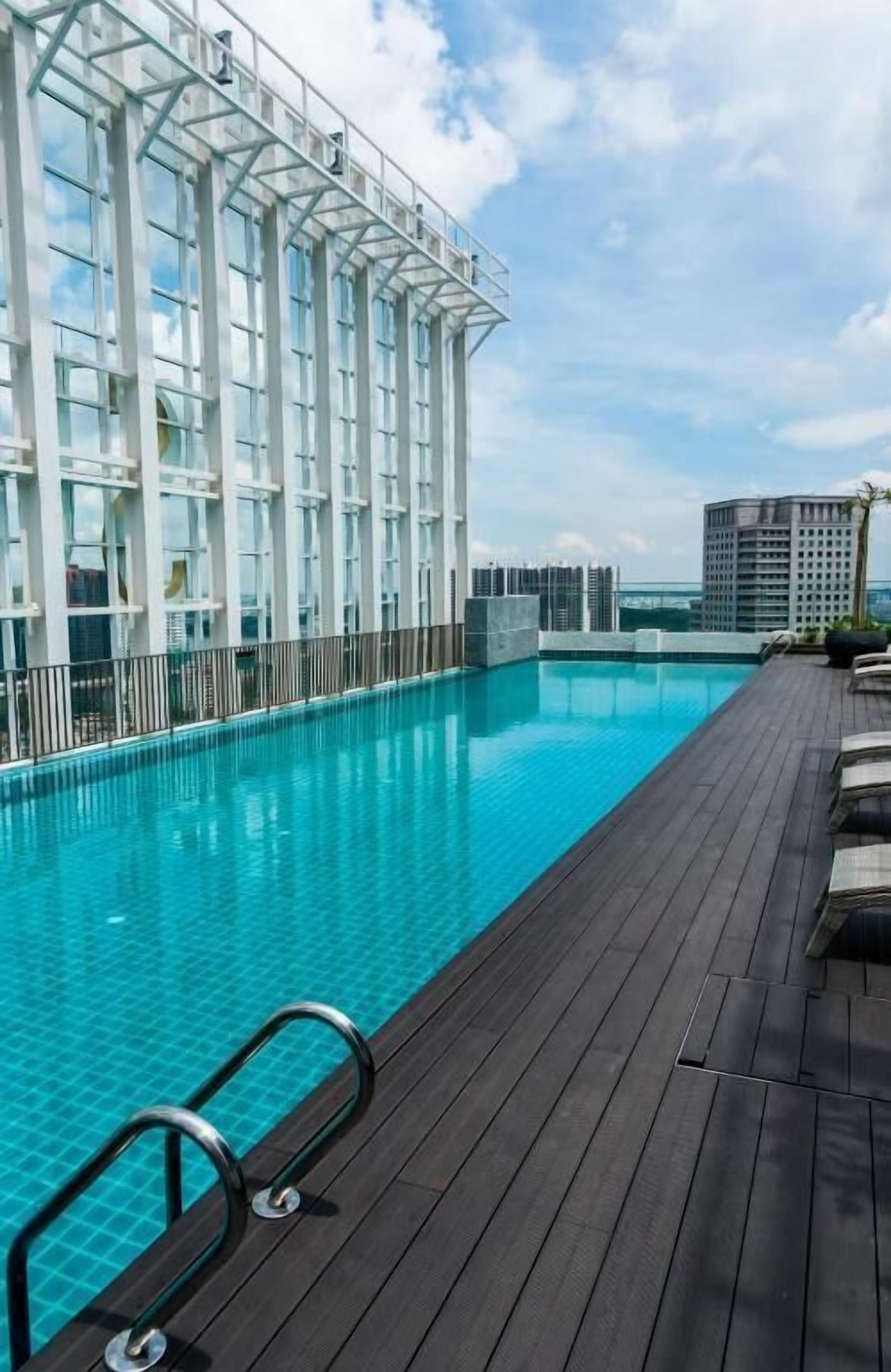 A rooftop swimming pool with a wooden deck, large windows, and a view of the city skyline.