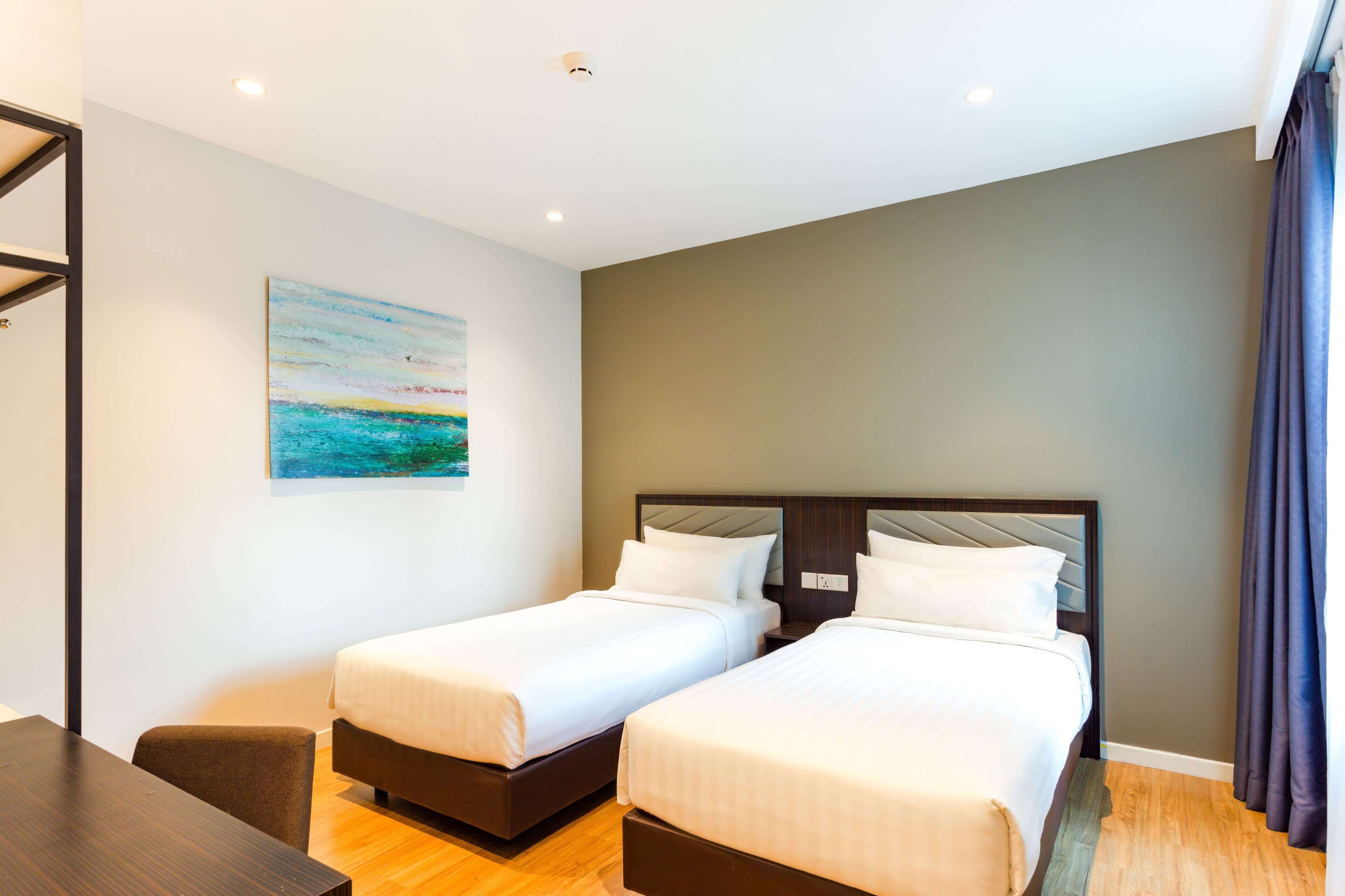 A hotel room with two beds, a wooden desk, and a painting on the wall.