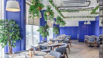 Interior modern d'un restaurant amb parets blaves, plantes penjants i taules i cadires ben ordenades.