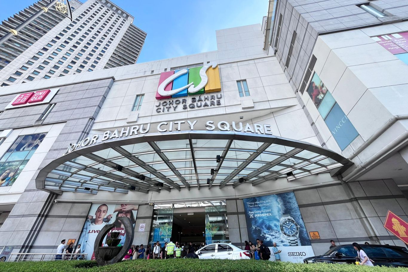 El edificio Bahru City Square con una entrada de vidrio moderna y anuncios de Levi's y Rolex.