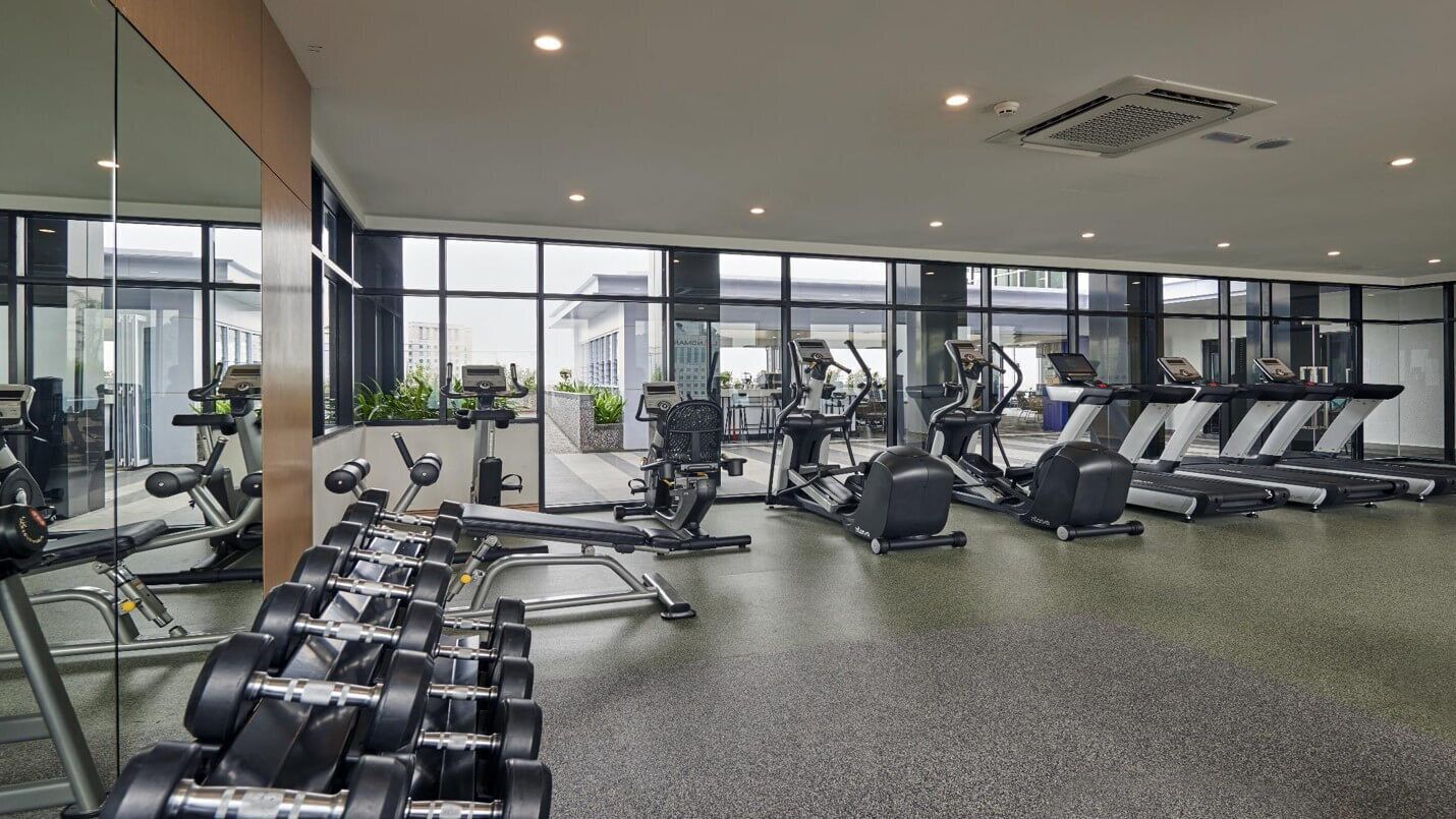 A modern gym with various exercise equipment, large windows, and a clean, spacious layout.