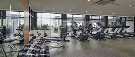 A modern gym with various exercise equipment, large windows, and a clean, spacious layout.