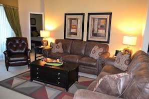A living room with a brown leather sofa, a matching armchair, a coffee table, and two framed artworks on the wall. - Ip60488 - The Shire at West Haven - 4 Bed 3 Baths Villa (Davenport)