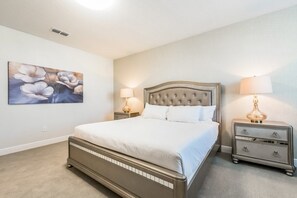 A bedroom with a large bed, two bedside tables with lamps, a wall-mounted painting, and a carpeted floor. - Aco245769 - The Encore Club Resort - 8 Bed 8 Baths Villa (Kissimmee)