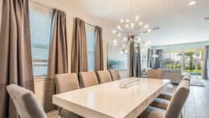 A modern dining area with a long table, multiple chairs, and a contemporary chandelier.