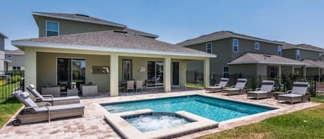 A residential building with a swimming pool, lounge chairs, and a hot tub.