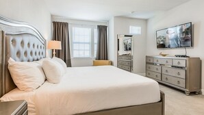 A hotel room with a large bed, a dresser, a television, and a window with curtains.