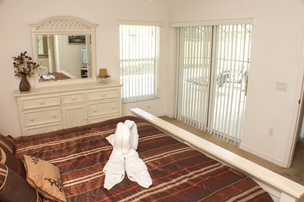 A bedroom with a bed, a dresser, a mirror, and a window with blinds.