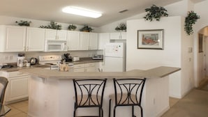 A kitchen with white cabinets, a microwave, a stove, a refrigerator, and two bar stools. - Ip60460 - Highgate at Legacy Park - 4 Bed 3 Baths Villa (Davenport)