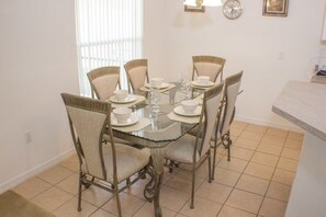 Un comedor con una mesa de vidrio rodeada por seis sillas, cada una con asiento y respaldo acolchados.