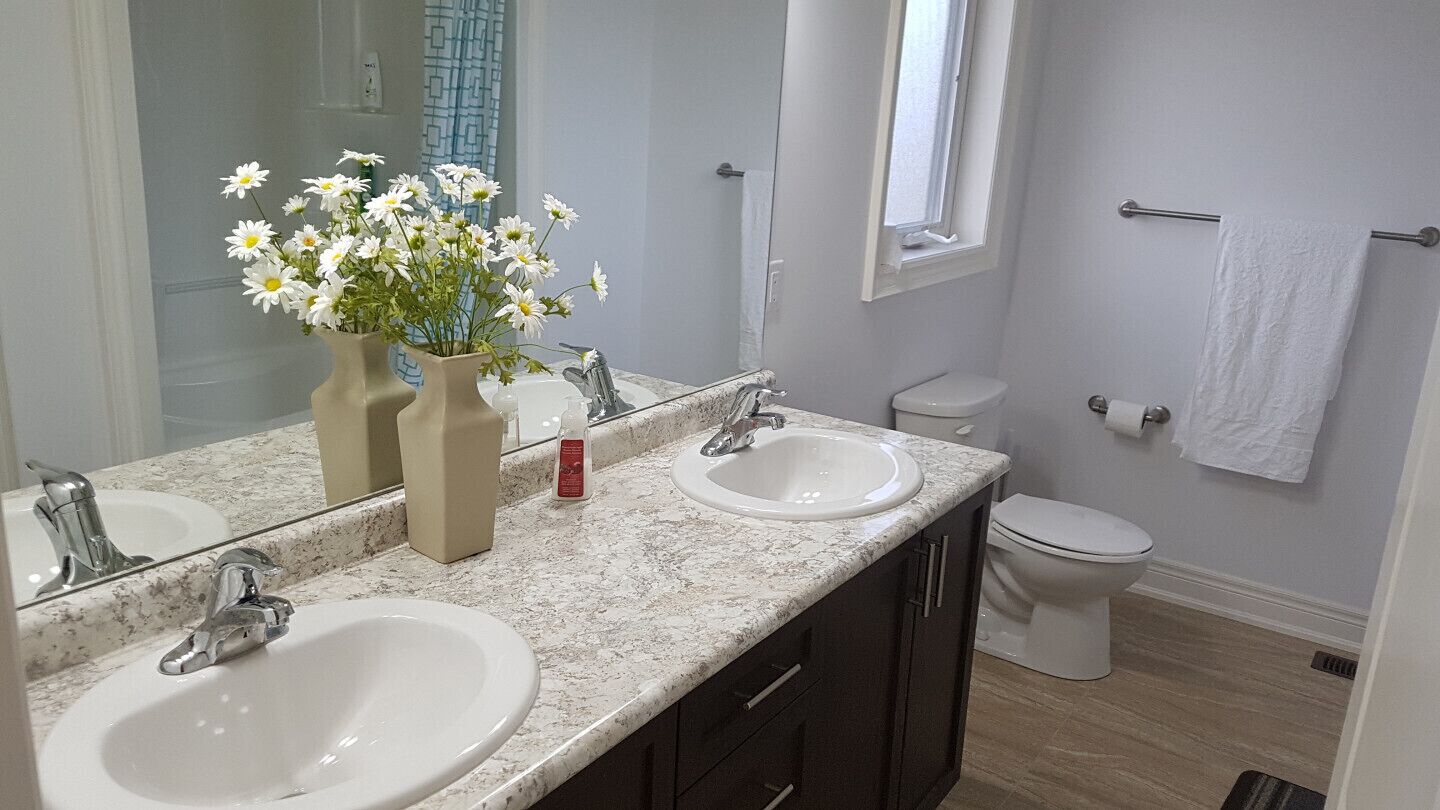 A bathroom with two sinks, a mirror, a toilet, and a window.