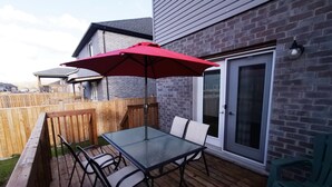 Eine Terrasse im Freien mit einem Glastisch und Stühlen, einem roten Sonnenschirm und einem Holzdeck.