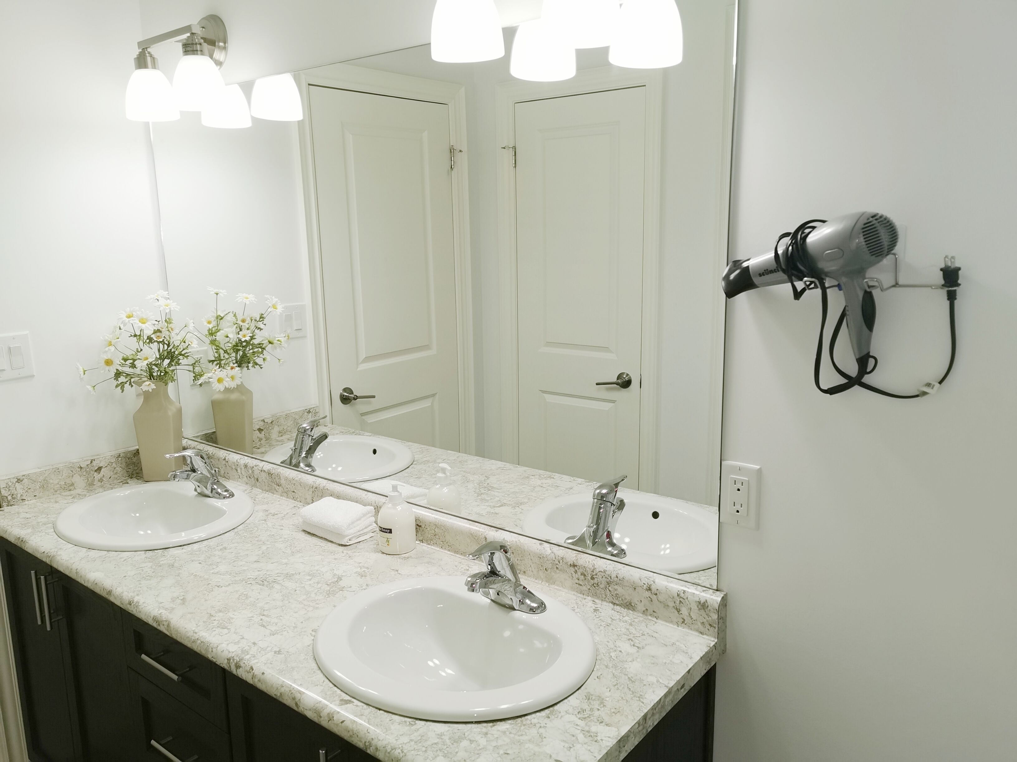 Une salle de bain avec deux lavabos, un grand miroir et un sèche-cheveux fixé au mur.