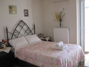 A neatly made bed with a floral bedspread, a bedside table with a lamp, and a vase with flowers on the wall.