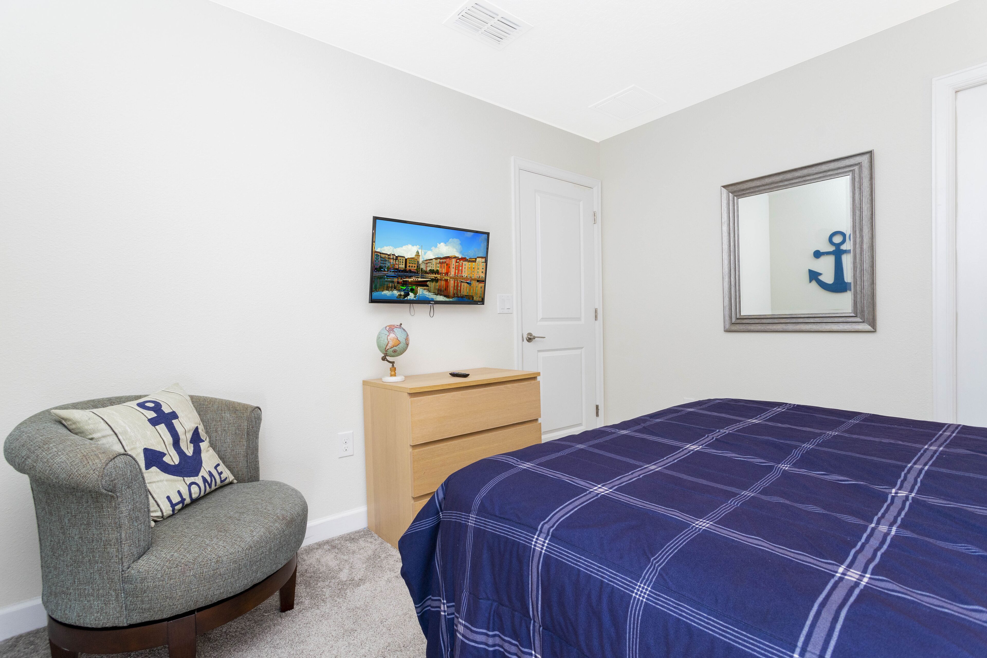 A bedroom with a bed, a chair, a dresser, a television, and a door.