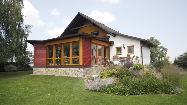 A house with a stone foundation, a red and yellow exterior, and a large glass window.