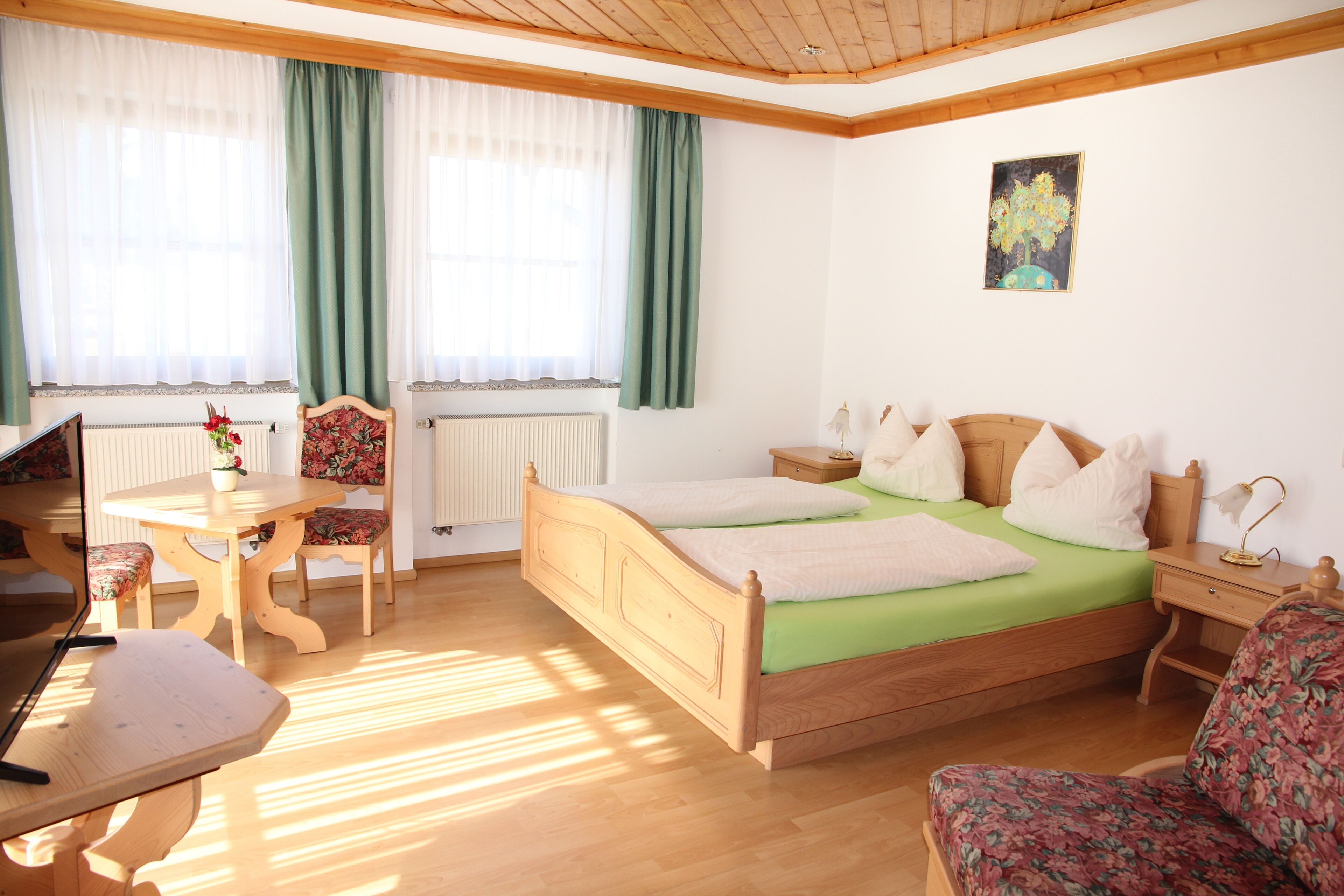 Ein Schlafzimmer mit einem hölzernen Bett, grüner Bettwäsche, einem Schreibtisch, einem Stuhl und einer Heizung.