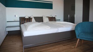 A modern bedroom with a large bed, a nightstand, a blue chair, and a wardrobe.