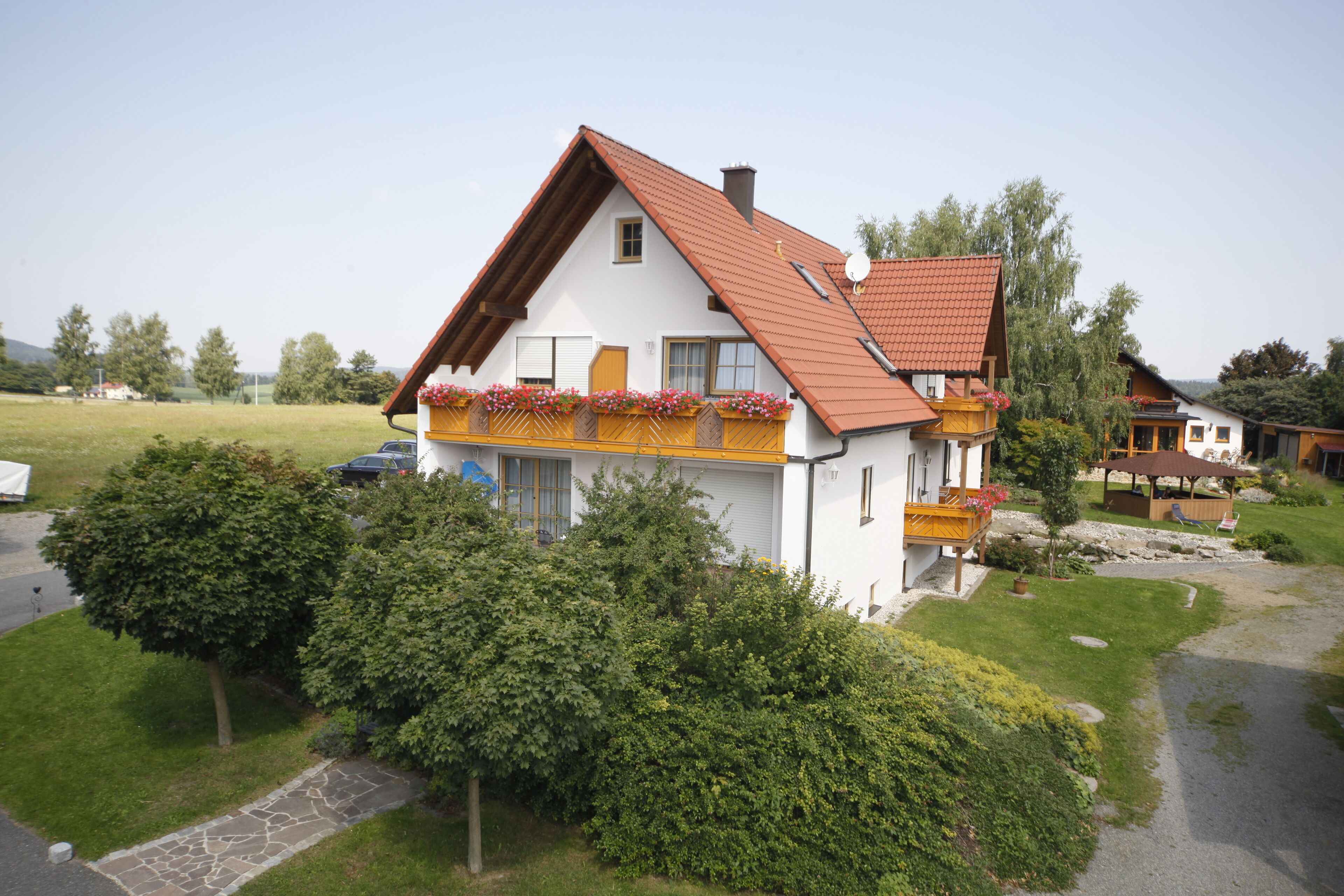 A two-story house with a sloped roof, a balcony with flowers, and a stone pathway leading to the entrance.