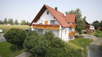 A two-story house with a sloped roof, a balcony with flowers, and a stone pathway leading to the entrance.