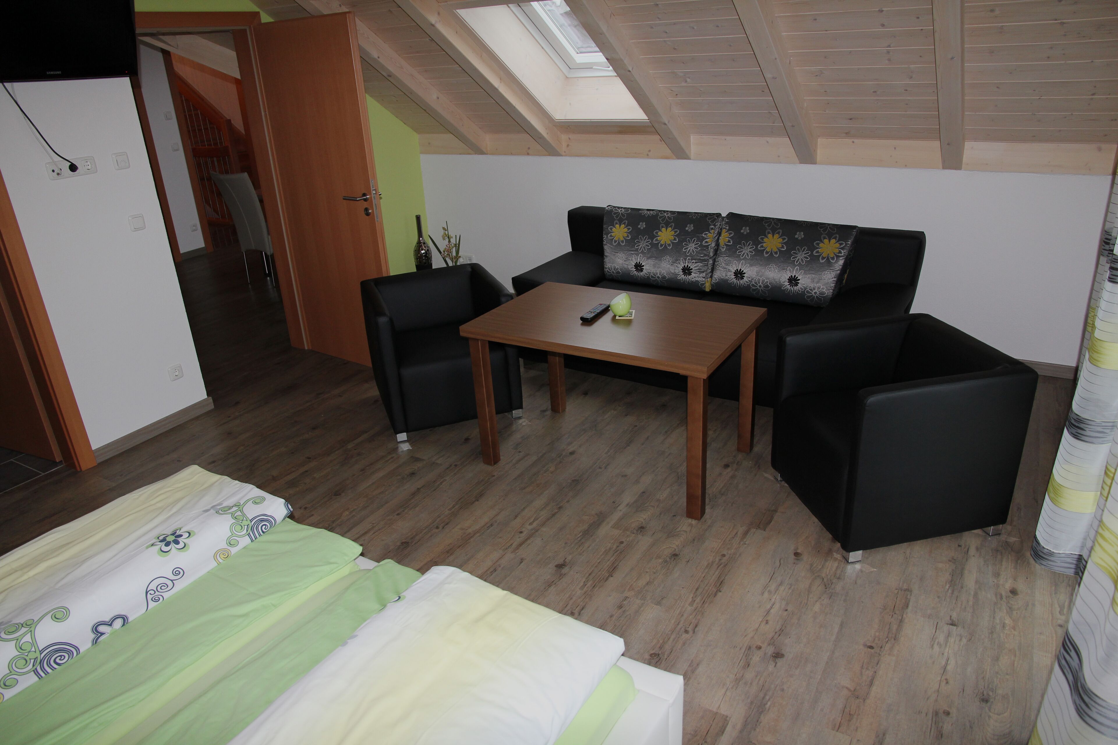 Une pièce comprenant un lit, un canapé, une table et une chaise. Un puits de lumière se trouve au-dessus du canapé.