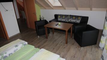 Une pièce comprenant un lit, un canapé, une table et une chaise. Un puits de lumière se trouve au-dessus du canapé.