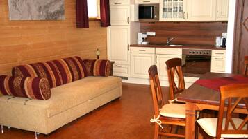Un salón acogedor con sofá y sillones, una mesa de comedor de madera y una cocina con armarios y electrodomésticos blancos.