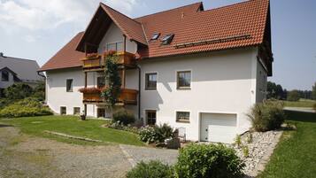 A two-story house with a sloped roof, a balcony with plants, and a gravel driveway.