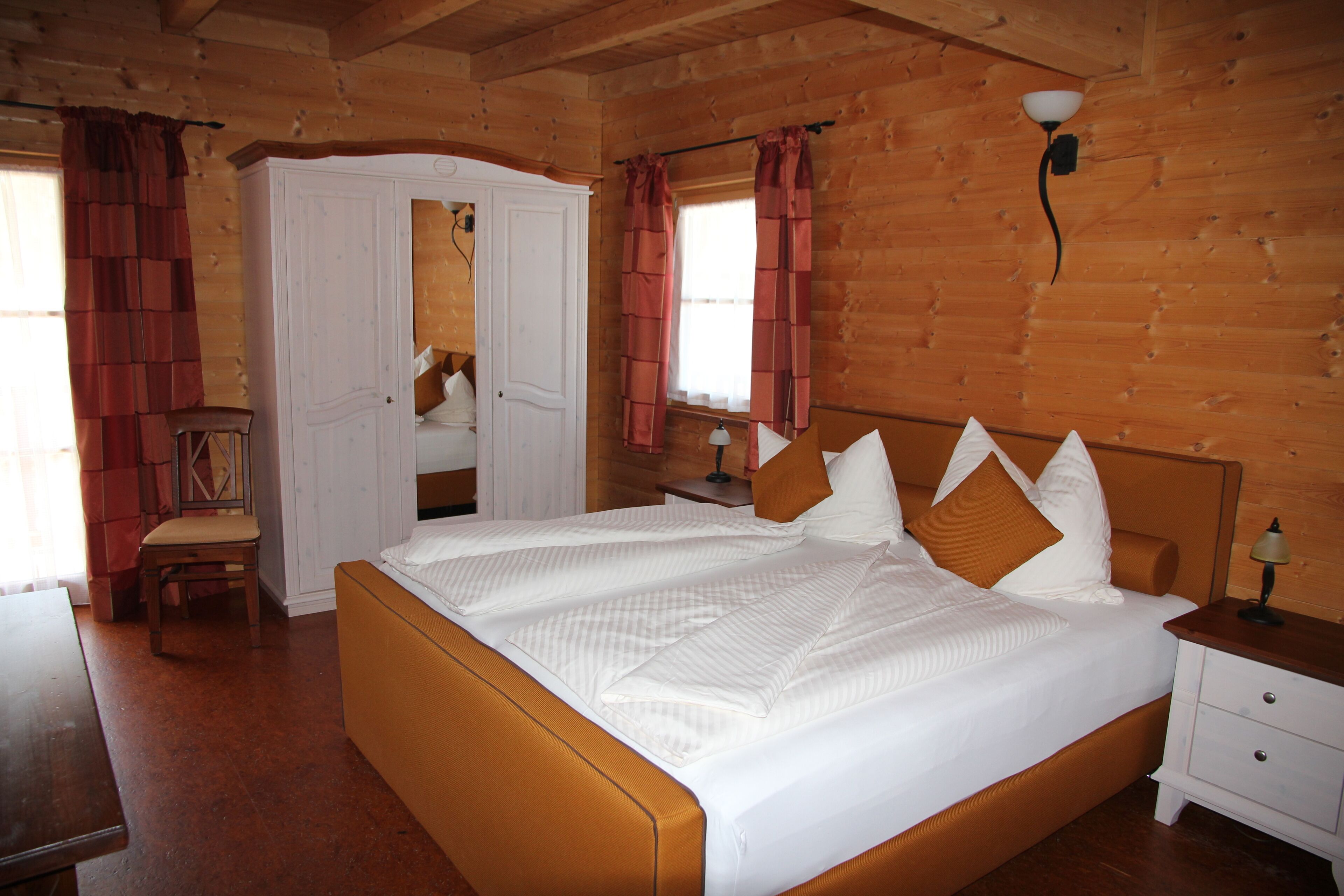 A wooden cabin bedroom with a bed, bedside table, and a chair.