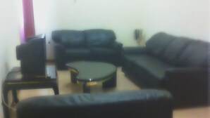A living room with a black sofa, a coffee table, and a TV on a stand. - Hotel América (Praia)
