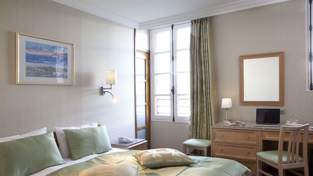 Een hotelkamer met een bed, bureau, stoel en een raam met gordijnen.