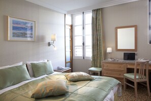 Ein Hotelzimmer mit Bett, Schreibtisch, Stuhl und einem Fenster mit Vorhängen.
