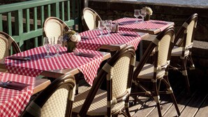 Een tafel gedekt met een rood-wit geruit tafelkleed, rieten stoelen en een uitzicht op een waterpartij.