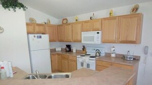A compact kitchen with wooden cabinets, a white refrigerator, a microwave, a stove, and a sink. - Ahr237 - Hamlets at West Haven - 4 Bed 3 Baths Villa (Davenport)