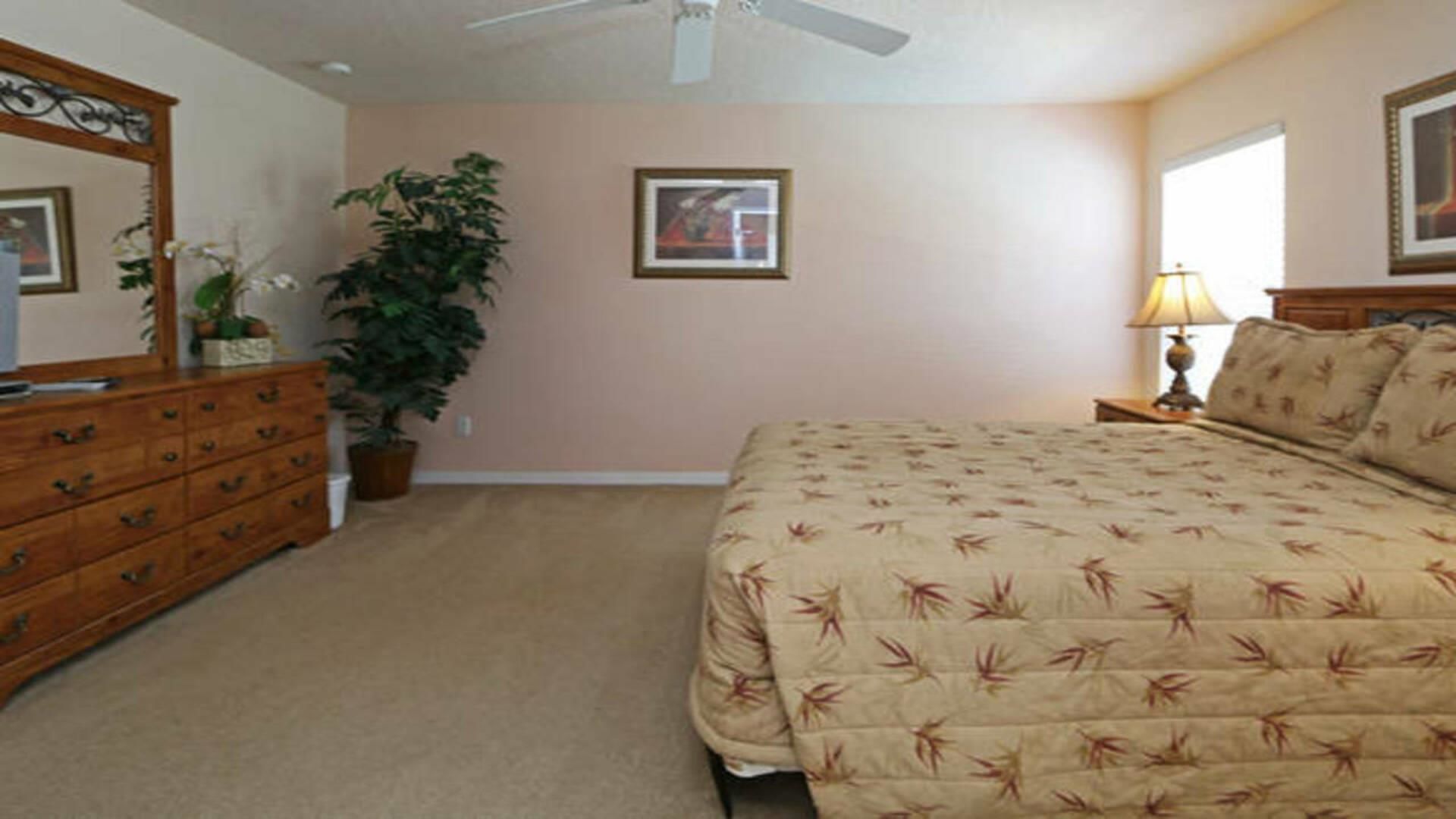 Quarto com cama, penteadeira, espelho, planta e quadro na parede.