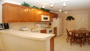 A kitchen with wooden cabinets, a microwave, a refrigerator, a stove, and a dining table with chairs. - Smw148 - Sandy Ridge - 3 Bed 3 Baths Villa (Davenport)