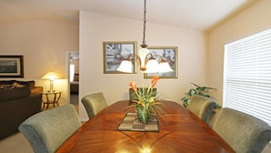 A dining room with a wooden table, chairs, a vase with flowers, and two wall-mounted lamps. - Smw148 - Sandy Ridge - 3 Bed 3 Baths Villa (Davenport)