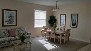 A living room with a sofa, a dining table with chairs, a coffee table, and a large plant.