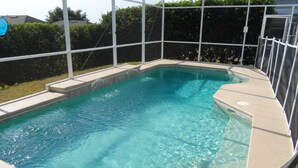 A rectangular swimming pool with clear blue water, surrounded by a white safety fence and a covered area.