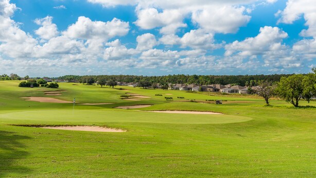 A golf course with bunkers, a flagstick, and a clear blue sky.
