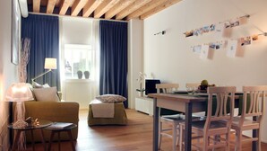 A cozy living room with a wooden ceiling, a sofa, a dining table with chairs, and a wall decorated with photos. - MAZZONI 15 MODERN FLAT BY VENICE TRAIN STATION (Venezia)