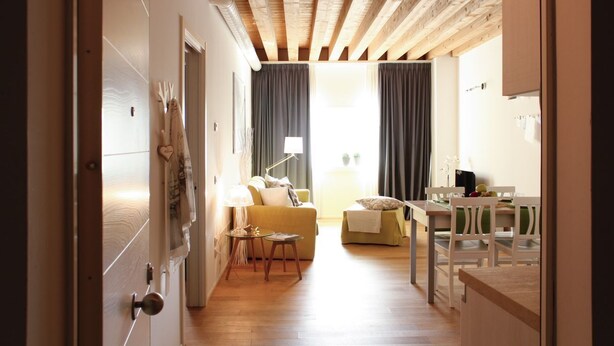 A modern interior with a wooden ceiling, a dining area with a table and chairs, a sofa, and a small side table with a lamp. - MAZZONI 15 MODERN FLAT BY VENICE TRAIN STATION (Venezia)