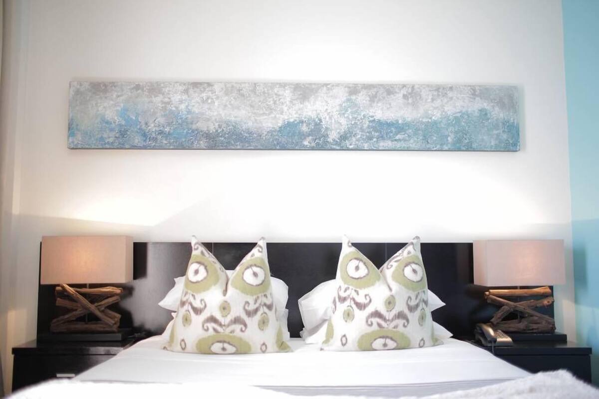 Une chambre d’hôtel avec un lit, deux tables de chevet, un tableau accroché au mur et des coussins décoratifs.
