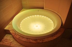 A circular bathtub with a light fixture in a bathroom with tiled walls and a marble countertop.